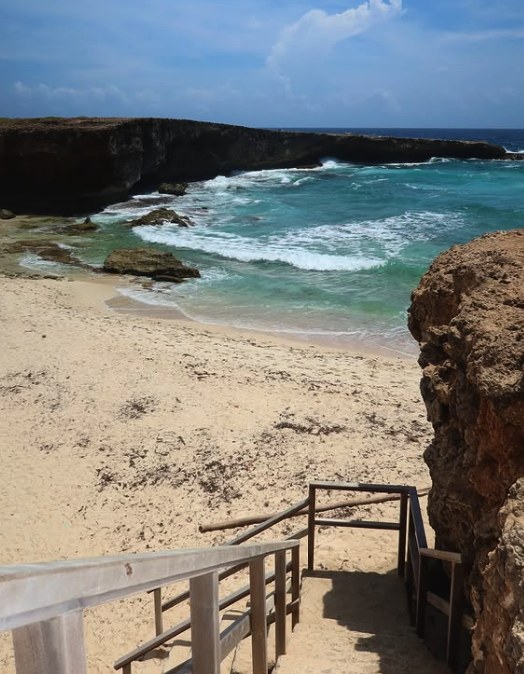The wooden steps down to Boca Prins, with surf breaking across the bay and the limestone headland behind it