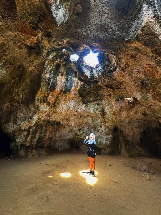 A visitor standing in a pool of daylight falling through two openings in a cave roof in Arikok National Park