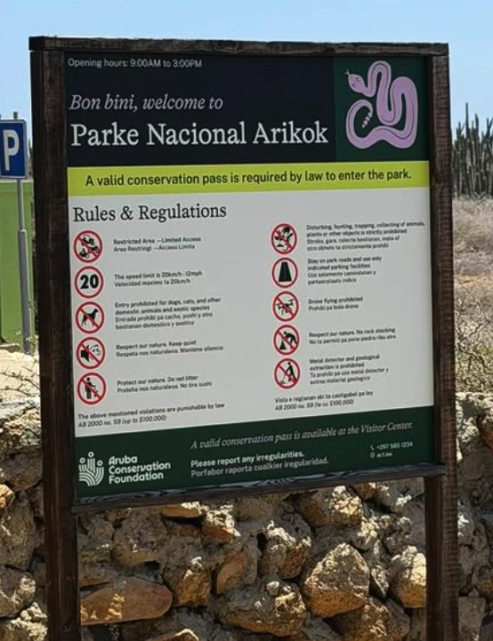 The Aruba Conservation Foundation board at a park entrance, listing the rules and stating that a valid conservation pass is required by law