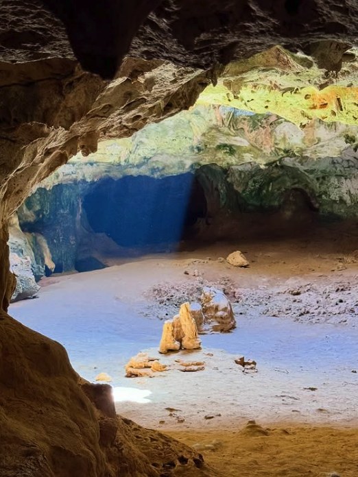 Inside Quadirikiri Cave, where daylight from the roof openings washes the far chamber blue and green