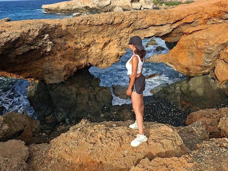 A walker standing under a low limestone arch on the windward shore, looking out at the surf